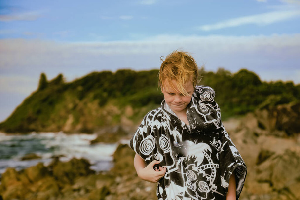 Boy wearing hooded towel after swimming standing on rocks at The Tanks tourist attraction at Forster, NSW Australia - Foto, Imagen