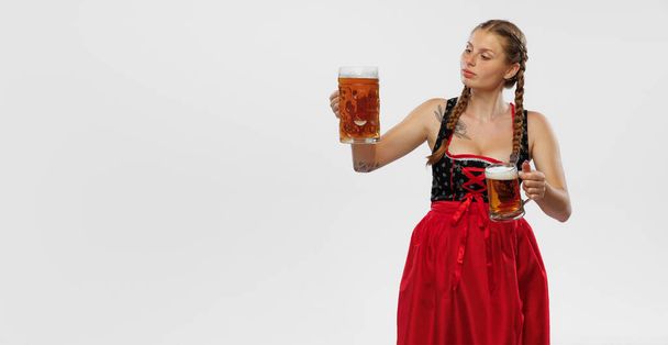 Oktoberfest vibe. Adorable smiling woman, waitress wearing a traditional Bavarian or german dirndl holding big mug of beer isolated on white background. Holiday, event, oktoberfest, festival - 写真・画像