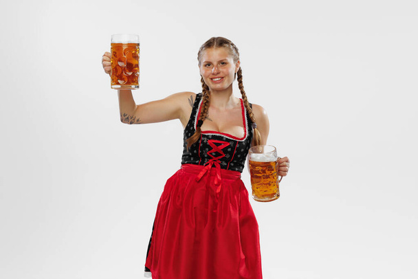 Taste. Oktoberfest vibe. Adorable smiling woman, waitress wearing a traditional Bavarian or german dirndl holding big mug of beer isolated on white background. Holiday, event, oktoberfest, festival - Φωτογραφία, εικόνα