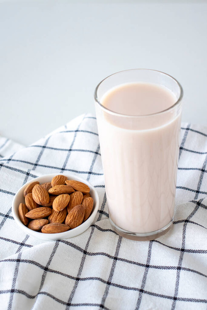 Almond milk in a glass with almonds on a white checkered cotton napkin. - Photo, image
