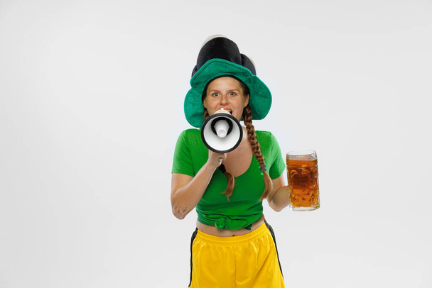 Shouting at megaphone. Happy excited woman in green yellow football kit holding beer mug and football ball supports favorite team. Emotions, fans, competition, sport, oktoberfest concept. St. Patrick - Foto, Bild