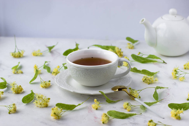Чай с липой в белой чашке на белом мраморном столе. Белый чайник с ароматным чаем - Фото, изображение
