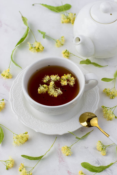 Tea with linden in a white cup on a white marble table. White teapot with aromatic tea - Foto, afbeelding