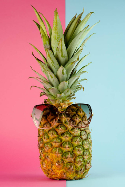 Pineapple with sunglasses. Summer vacation concept on pink and blue background - Fotó, kép