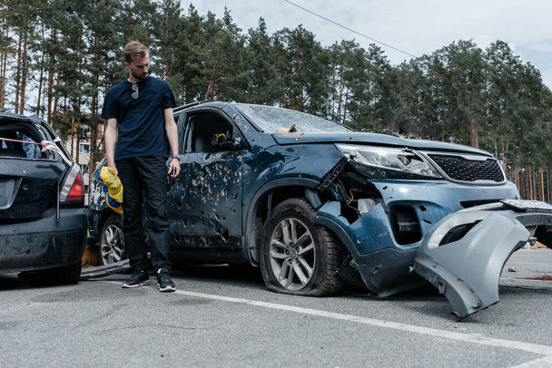 Man stands near shot damaged car riddled with bullets. Car shot by the Russian military during the evacuation of civilians. Shrapnel and bullet holes in the body of the car. War in Ukraine and Europe. - 写真・画像