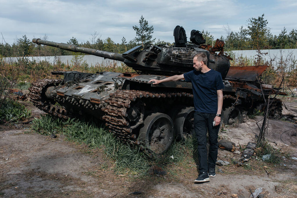 Man stands near destroyed and burned by the Ukrainian army russian tank near Kyiv. Russian military invasion in Ukraine. War in Ukraine and Europe. - 写真・画像