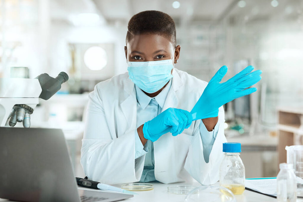 Shot of a young scientist sitting alone in her laboratory and putting surgical gloves on. - Foto, imagen