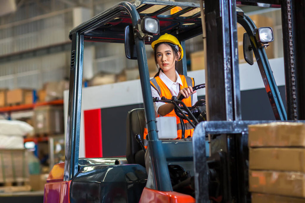 smiling delivery worker with forklift in uniform standing in warehouse - Foto, afbeelding