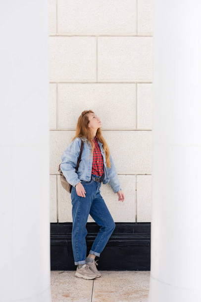 A woman in a casual denim outfit stands in the opening between the columns against light wall with large tiles. - Photo, Image