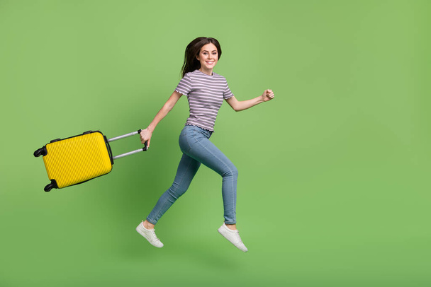Full length body size view of attractive girl jumping with bag running flight comfort airline isolated on bright green color background. - Foto, afbeelding