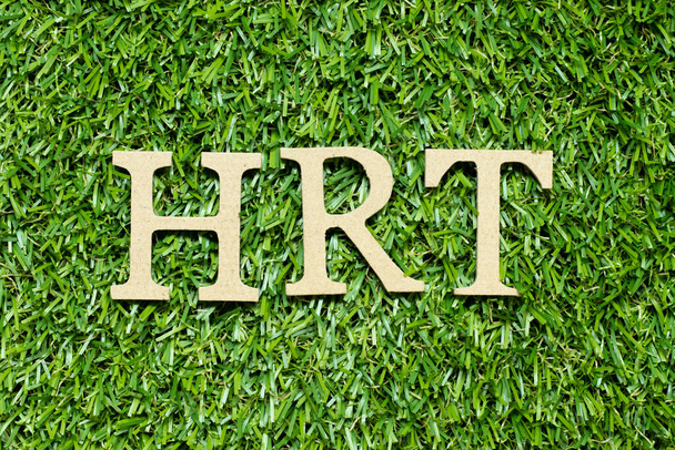 Wood alphabet letter in word HRT (Abbreviation of Hormone replacement therapy) on green grass background - Foto, Imagem