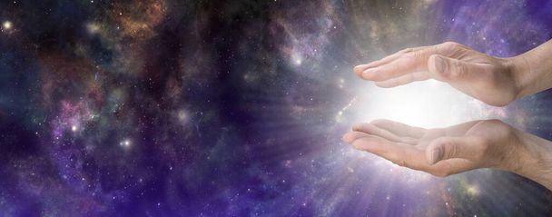 Heavenly Life Force Concept sky Banner - male cupped hands with bright white light energy radiating outwards against wide dark celestial deep space  sky background with copy space - Fotografie, Obrázek