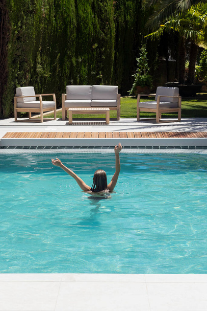 Vertical view of young unrecognizabel woman enjoying the refreshing time in the swimming pool in hot summer day in the garden - Foto, immagini