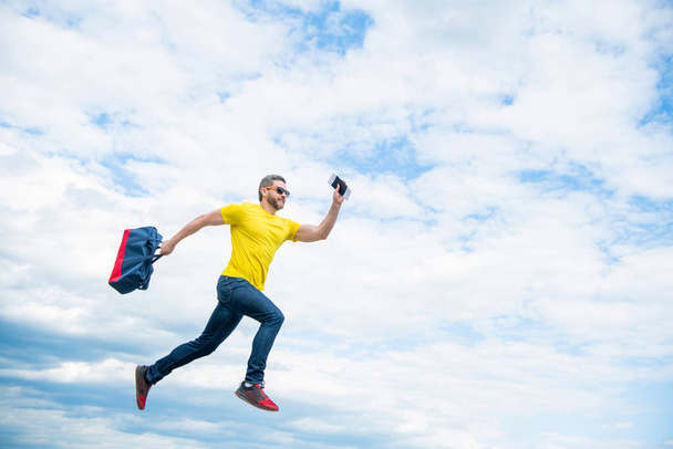 Energetic guy running with travel bag midair sky background, copy space. - Photo, Image