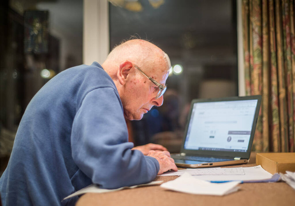Vanha mies 93 vuotta ottaa vaikeuksia käyttää tietokonetta tarkistaa hänen taloutensa verkossa, erittäin haastavaa vanhuksille. - Valokuva, kuva
