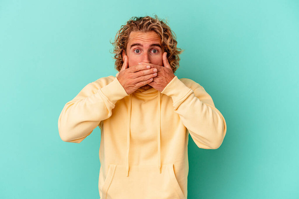 Giovane uomo caucasico isolato su sfondo blu che copre la bocca con le mani cercando preoccupato. - Foto, immagini