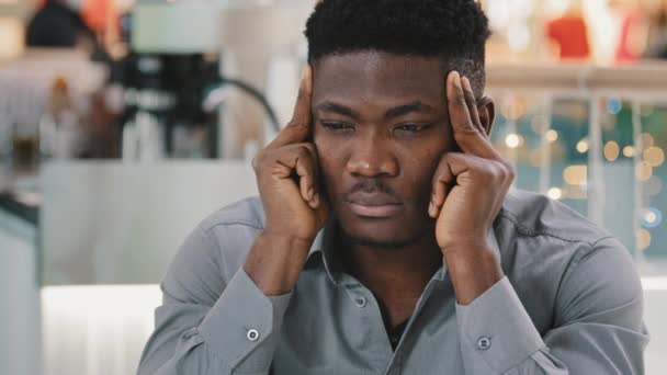 Zbliżenie smutny niezdrowy Afrykanin amerykański człowiek tarcie świątyń czuje silny ból głowy Cierpienie na objawy migreny martwi młody człowiek doświadcza bolesne uczucie przewlekłego bólu - Materiał filmowy, wideo