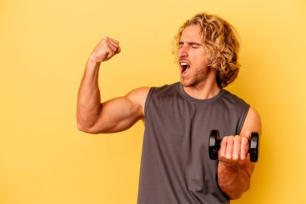 young sport man making weightlifting isolated on yellow background raising fist after a victory, winner concept. - Photo, image