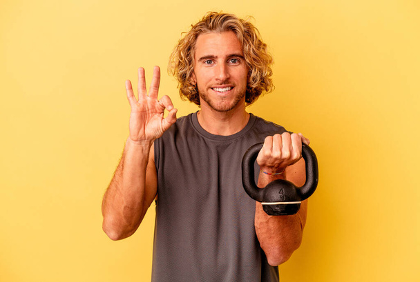 young sport man making weightlifting isolated on yellow background cheerful and confident showing ok gesture. - Fotografie, Obrázek