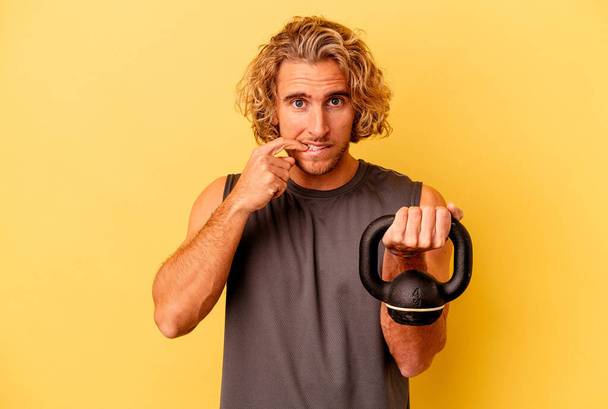 young sport man making weightlifting isolated on yellow background biting fingernails, nervous and very anxious. - Фото, изображение
