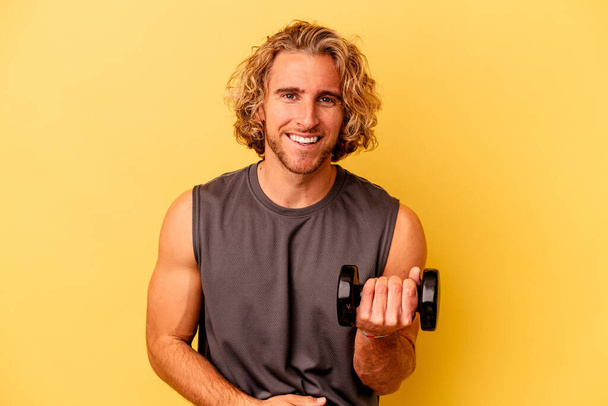 young sport man making weightlifting isolated on yellow background laughing and having fun. - Photo, image