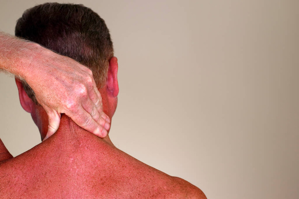 Adult male rubbing the back side of his neck with his hand as seen from a rear view close-up. Adult mature male 50 - 59 years massaging the back of his neck to help relive stress and tensio - Zdjęcie, obraz