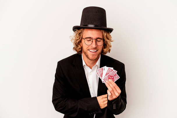 Young magician caucasian man holding magic cards isolated on white background laughing and having fun. - Zdjęcie, obraz