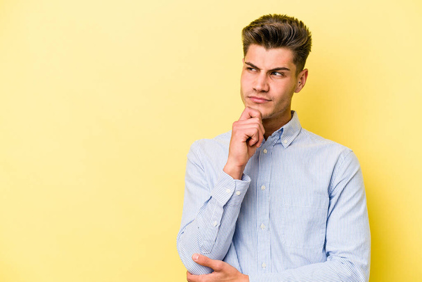 Young caucasian man isolated on yellow background looking sideways with doubtful and skeptical expression. - Foto, imagen