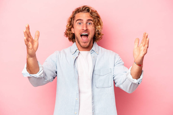 Young caucasian man isolated on pink background celebrating a victory or success, he is surprised and shocked. - Photo, Image