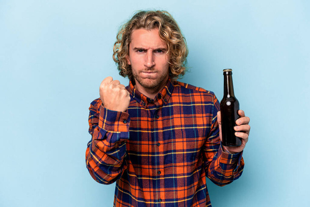 Young caucasian man holding beer isolated on white background showing fist to camera, aggressive facial expression. - 写真・画像