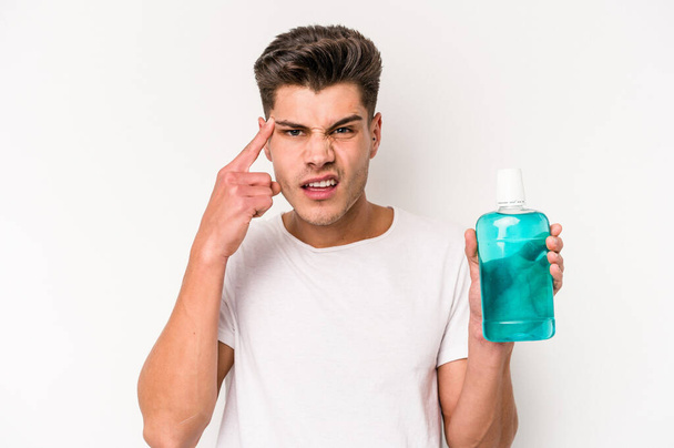Young caucasian man holding mouthwash isolated on white background showing a disappointment gesture with forefinger. - Photo, Image