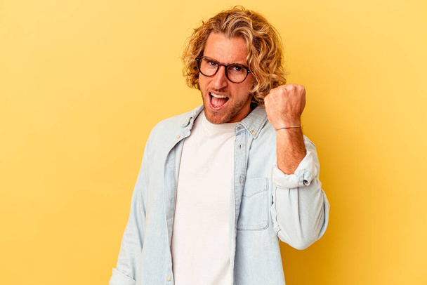 Young caucasian man isolated on yellow background celebrating a victory, passion and enthusiasm, happy expression. - Photo, Image