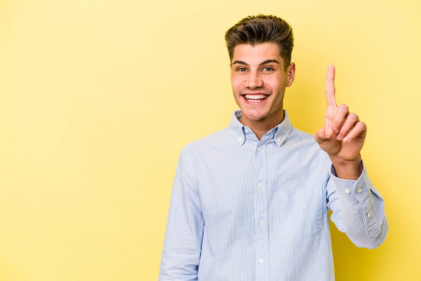 Νεαρός καυκάσιος άνδρας απομονωμένος σε κίτρινο φόντο, δείχνει το νούμερο ένα με δάχτυλο.. - Φωτογραφία, εικόνα