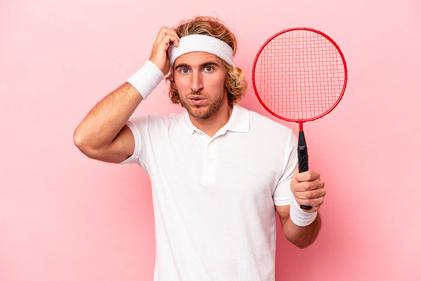 Giovane uomo caucasico giocare badminton isolato su sfondo rosa essere scioccato, ha ricordato importante incontro. - Foto, immagini