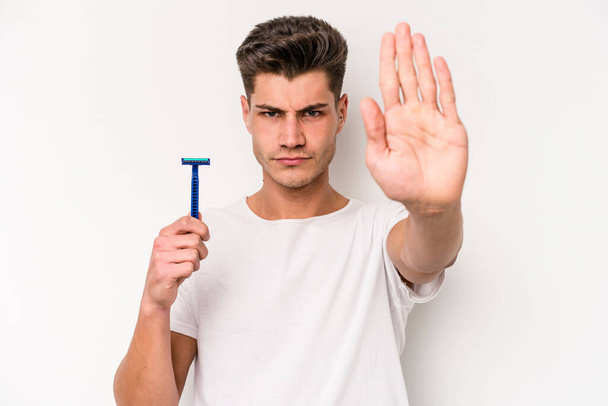 Young caucasian man shaving his beard isolated on white background standing with outstretched hand showing stop sign, preventing you. - Fotografie, Obrázek