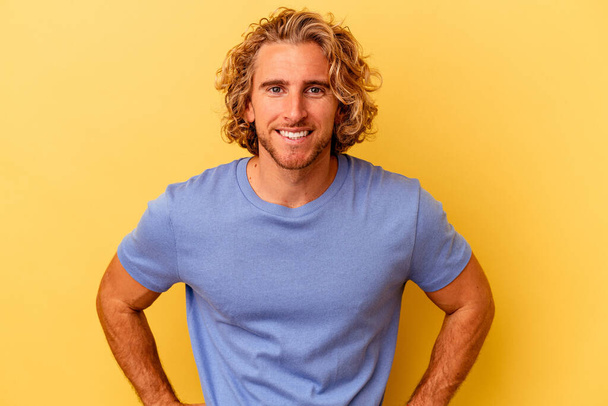 Young caucasian man isolated on yellow background confident keeping hands on hips. - Photo, Image