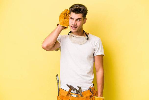 Young electrician caucasian man isolated on yellow background trying to listening a gossip. - Foto, afbeelding