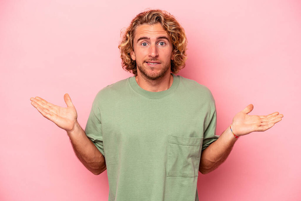 Young caucasian man isolated on pink background confused and doubtful shrugging shoulders to hold a copy space. - Photo, Image