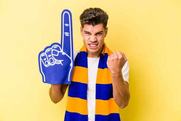 Young sports fan man isolated on yellow background showing fist to camera, aggressive facial expression. - Valokuva, kuva