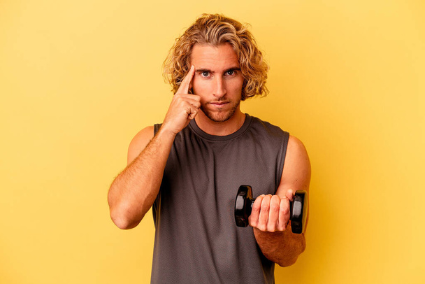 young sport man making weightlifting isolated on yellow background pointing temple with finger, thinking, focused on a task. - Foto, Bild