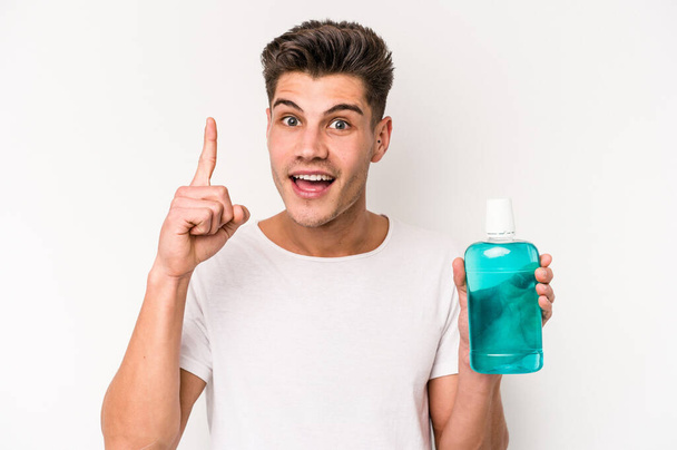 Young caucasian man holding mouthwash isolated on white background having an idea, inspiration concept. - Photo, image