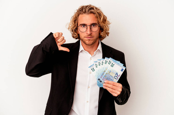 Fiatal kaukázusi üzletember, fehér háttérrel izolált bankjegyekkel, ami egy ellenszenves gesztust mutat, hüvelykujjal lefelé. A nézeteltérés fogalma. - Fotó, kép