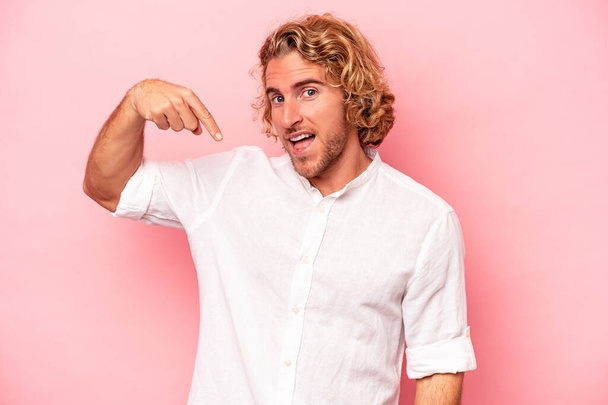 Young caucasian man isolated on pink background person pointing by hand to a shirt copy space, proud and confident - Фото, изображение