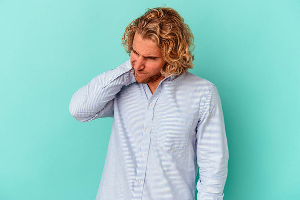 Young caucasian man isolated on blue background having a neck pain due to stress, massaging and touching it with hand. - Photo, image
