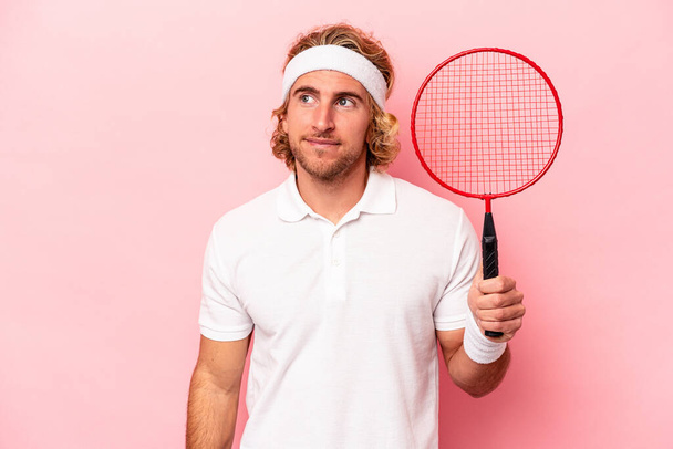 Young caucasian man playing badminton isolated on pink background dreaming of achieving goals and purposes - Photo, Image