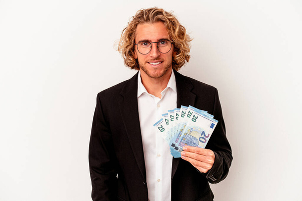 młody biały biznes człowiek trzymając banknoty odizolowane na białym tle szczęśliwy, uśmiechnięty i wesoły. - Zdjęcie, obraz