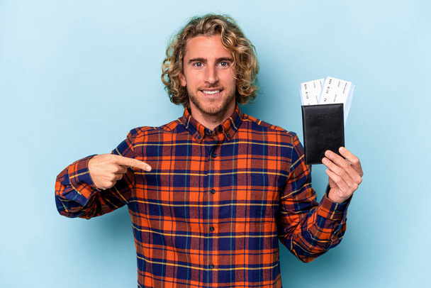 Young caucasian man holding a passport isolated on blue background person pointing by hand to a shirt copy space, proud and confident - Photo, image