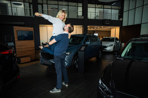 Happy caucasian couple hugging while buying a new car in a car dealership - Foto, imagen