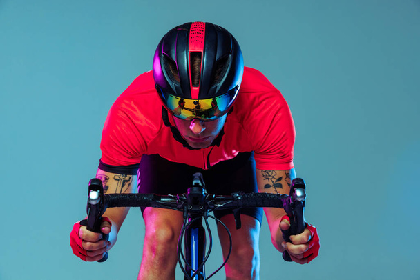 Champion. Studio shot of professional cyclist in red sports uniform, goggles and a helmet on a blue background. Concept of active life, rest, travel, energy, sport. Copy space for ad - Fotoğraf, Görsel