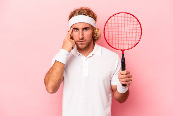 Junger kaukasischer Mann spielt Badminton isoliert auf rosa Hintergrund und zeigt mit dem Finger auf die Schläfe, denkt nach, konzentriert sich auf eine Aufgabe. - Foto, Bild